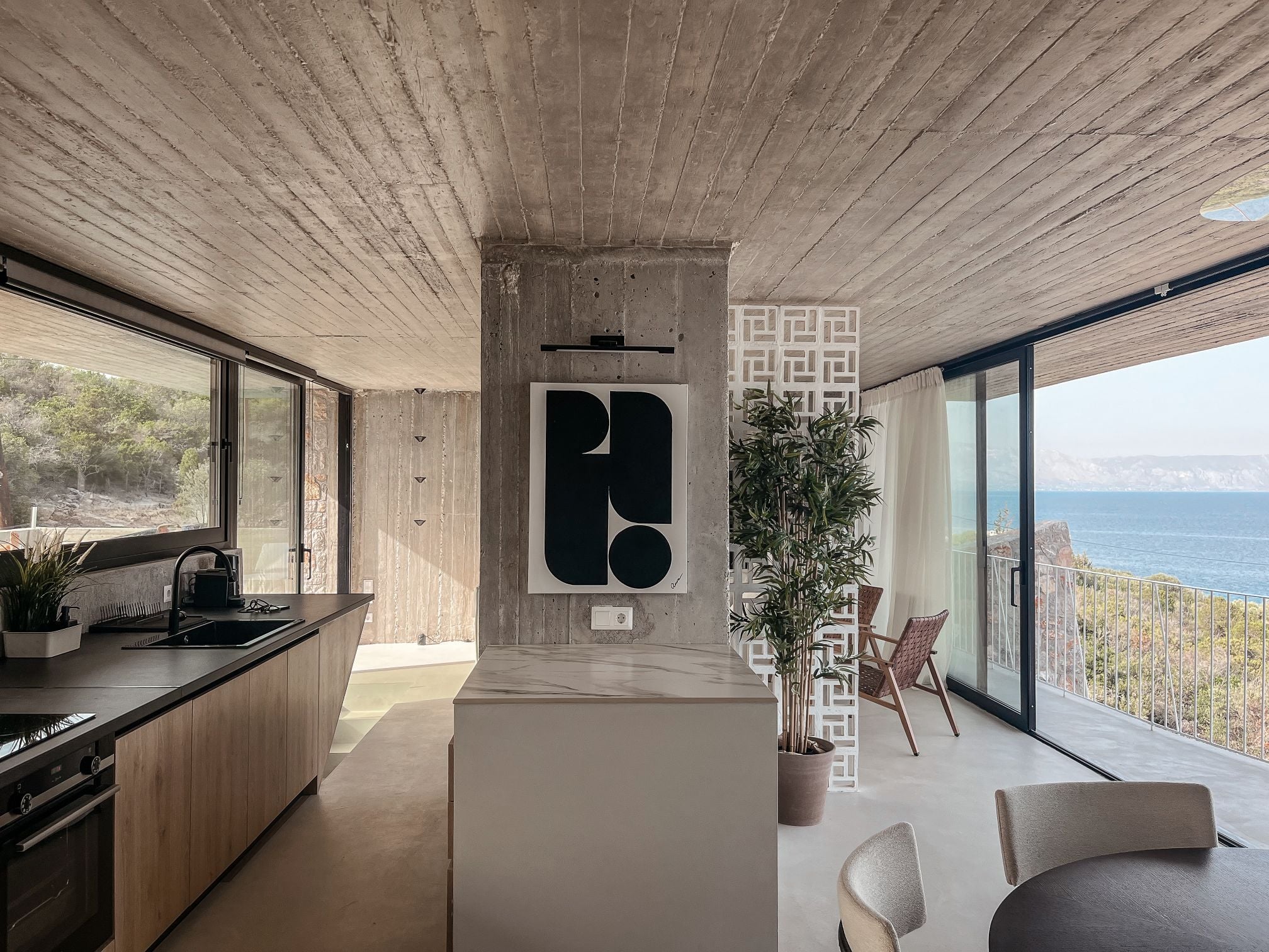Open-plan kitchen with a pale island, concrete ceiling and sea views — Amoni