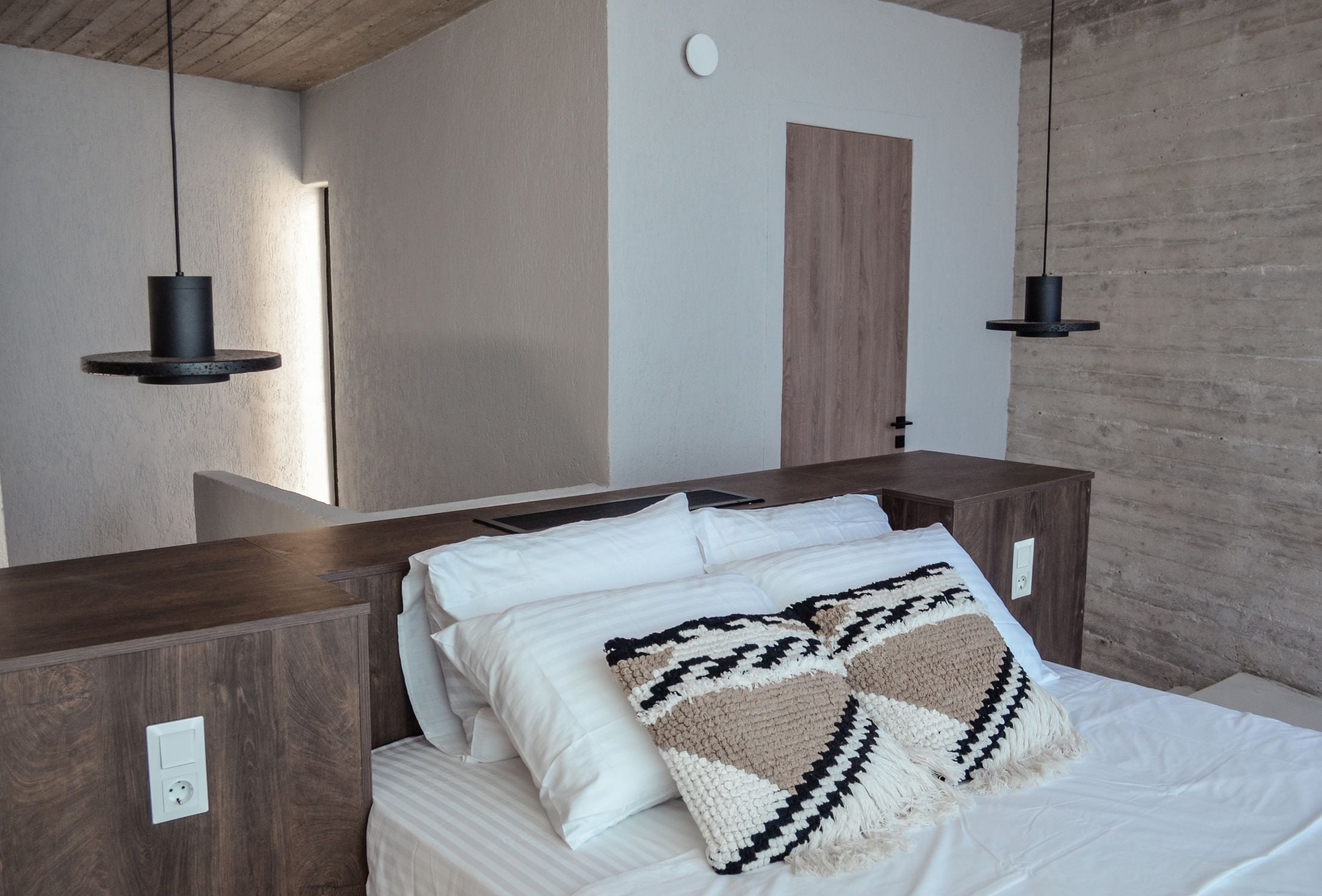 Bedroom with white bedding and dark pendant lights beside the bed — Amoni