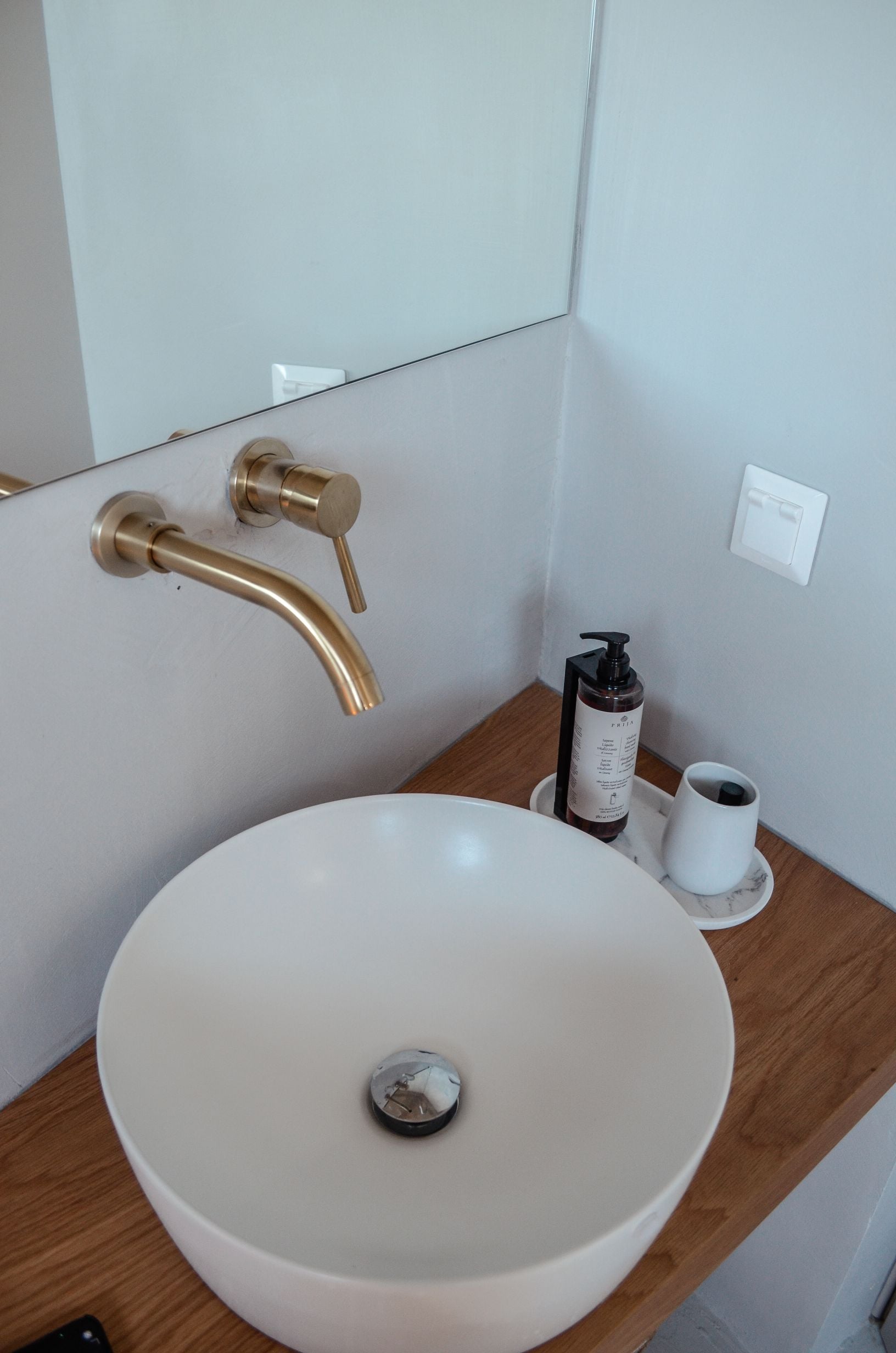Round white basin with a metal tap on a timber vanity — Amoni