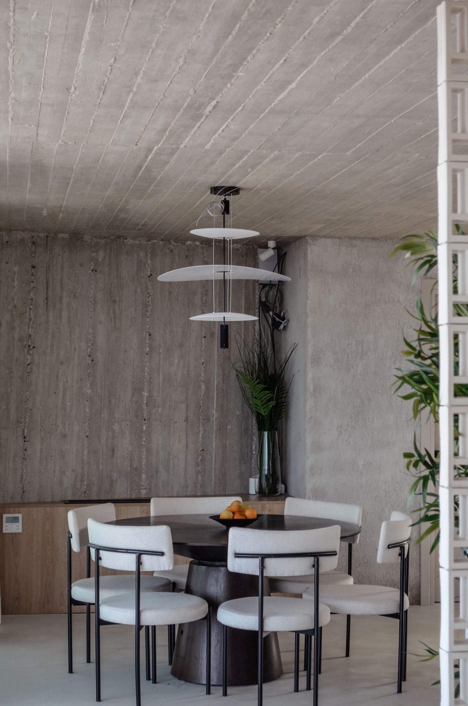 Dining area with a round table beneath layered pendant lighting — Amoni