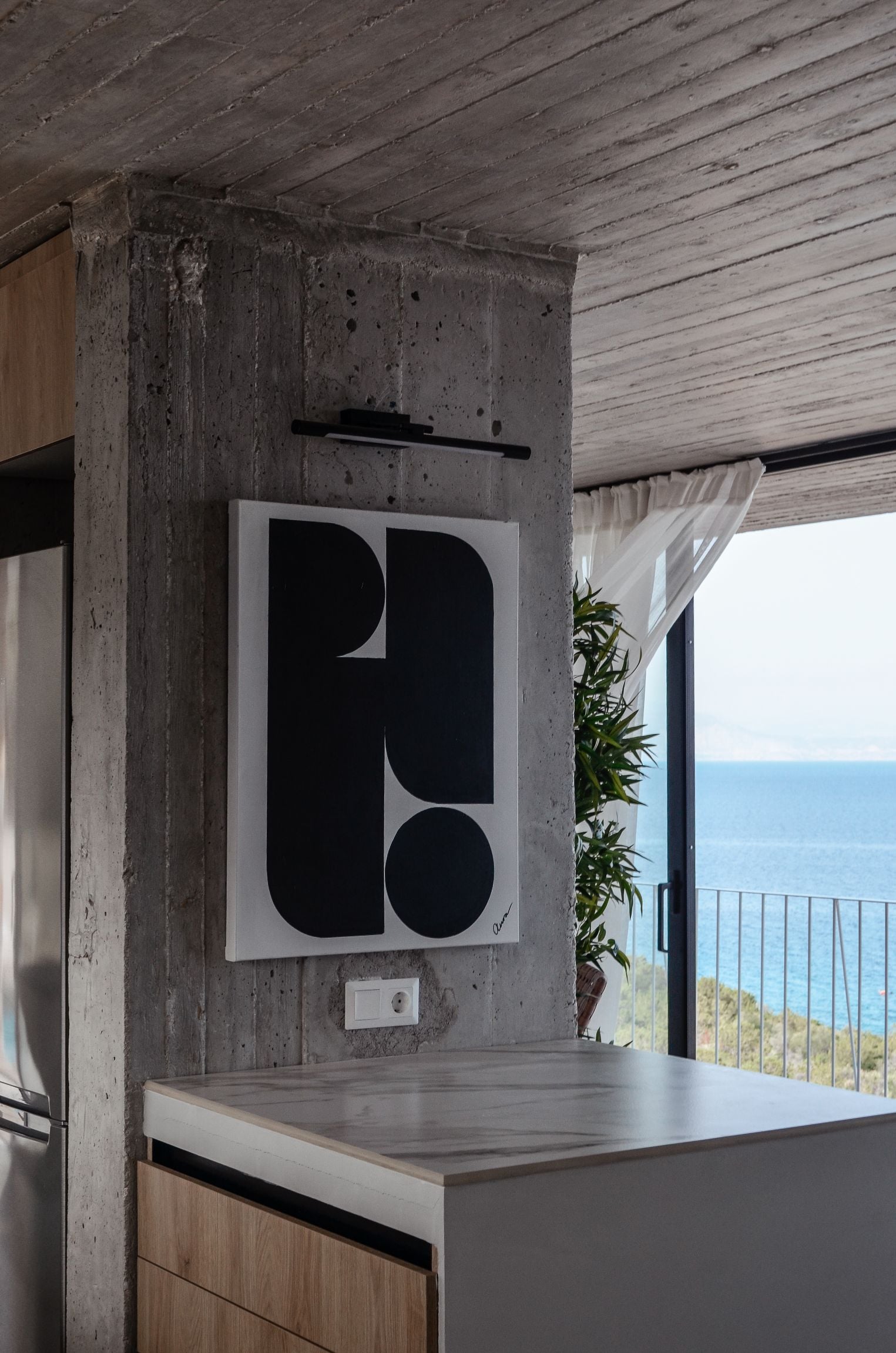 Dark sculptural artwork beside a large window overlooking the sea — Amoni