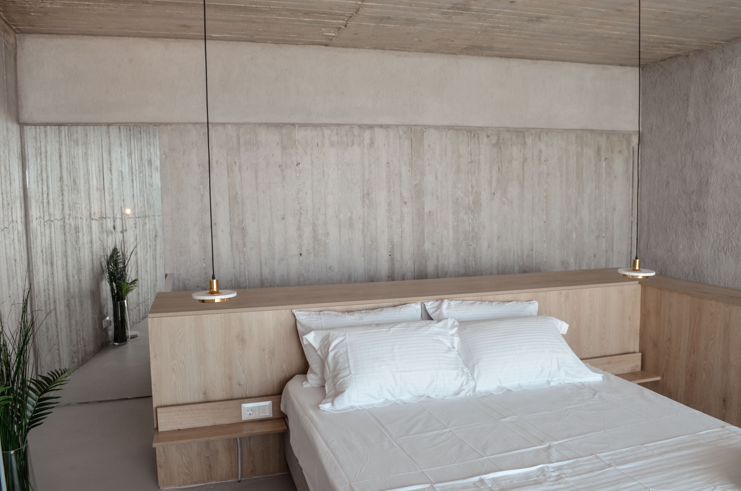 White bed against a concrete feature wall with pale overhead cabinetry — Amoni
