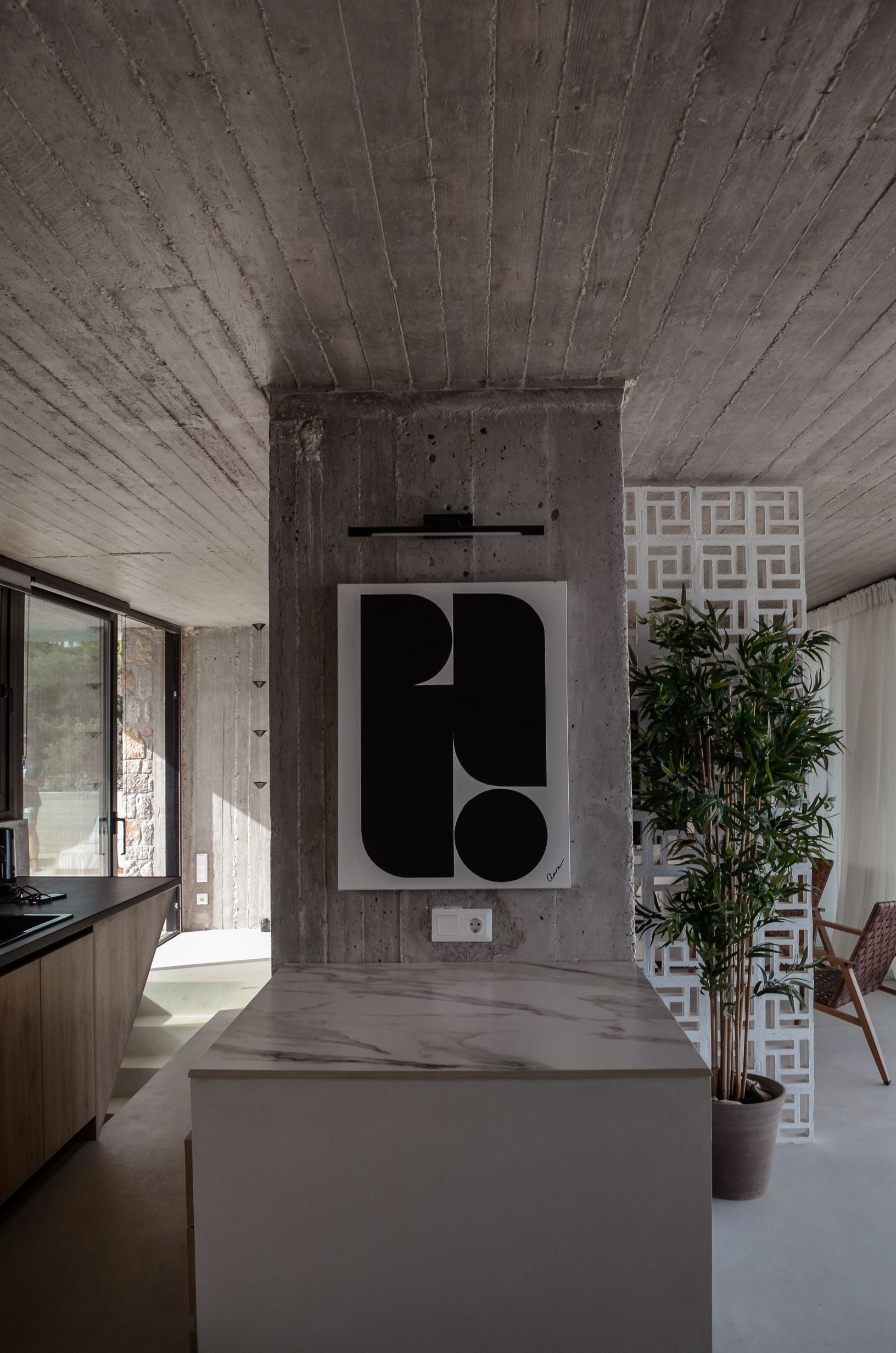 Kitchen island beneath exposed concrete beams beside a coastal view — Amoni