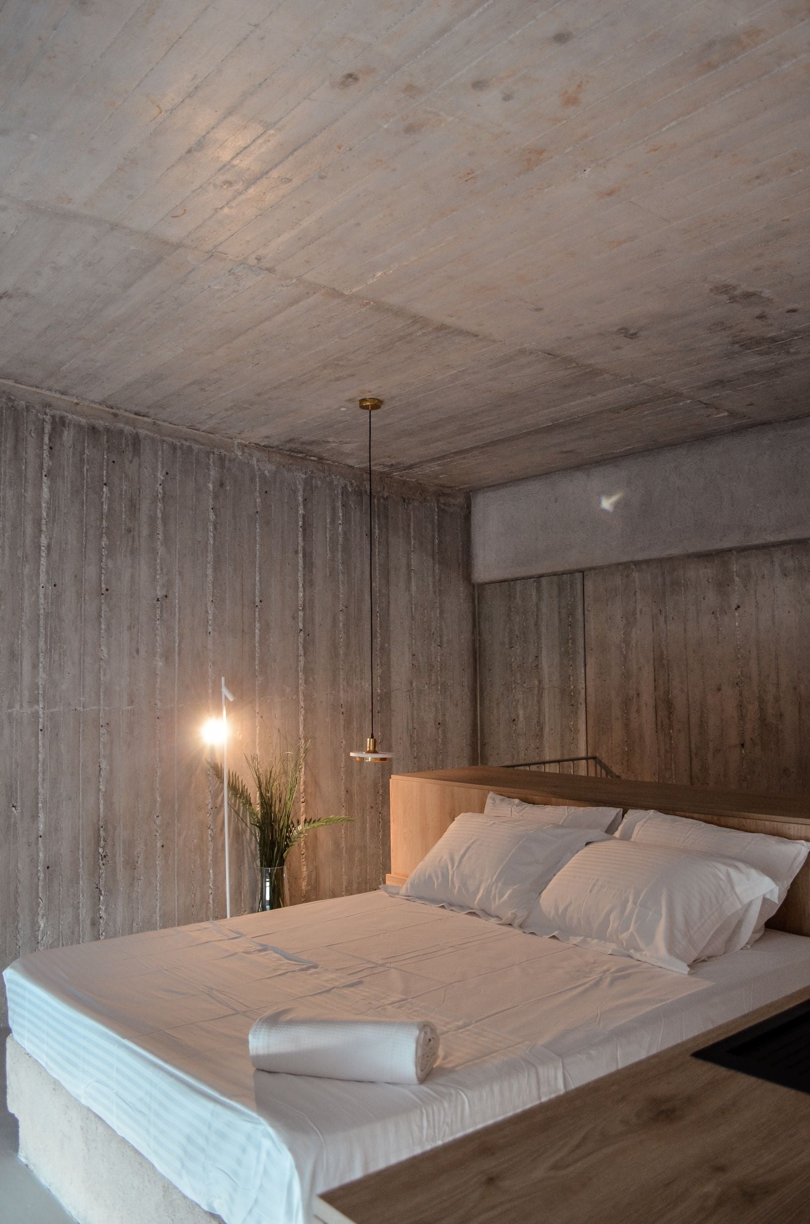 Concrete bedroom with warm bedside lights and timber cabinetry — Amoni