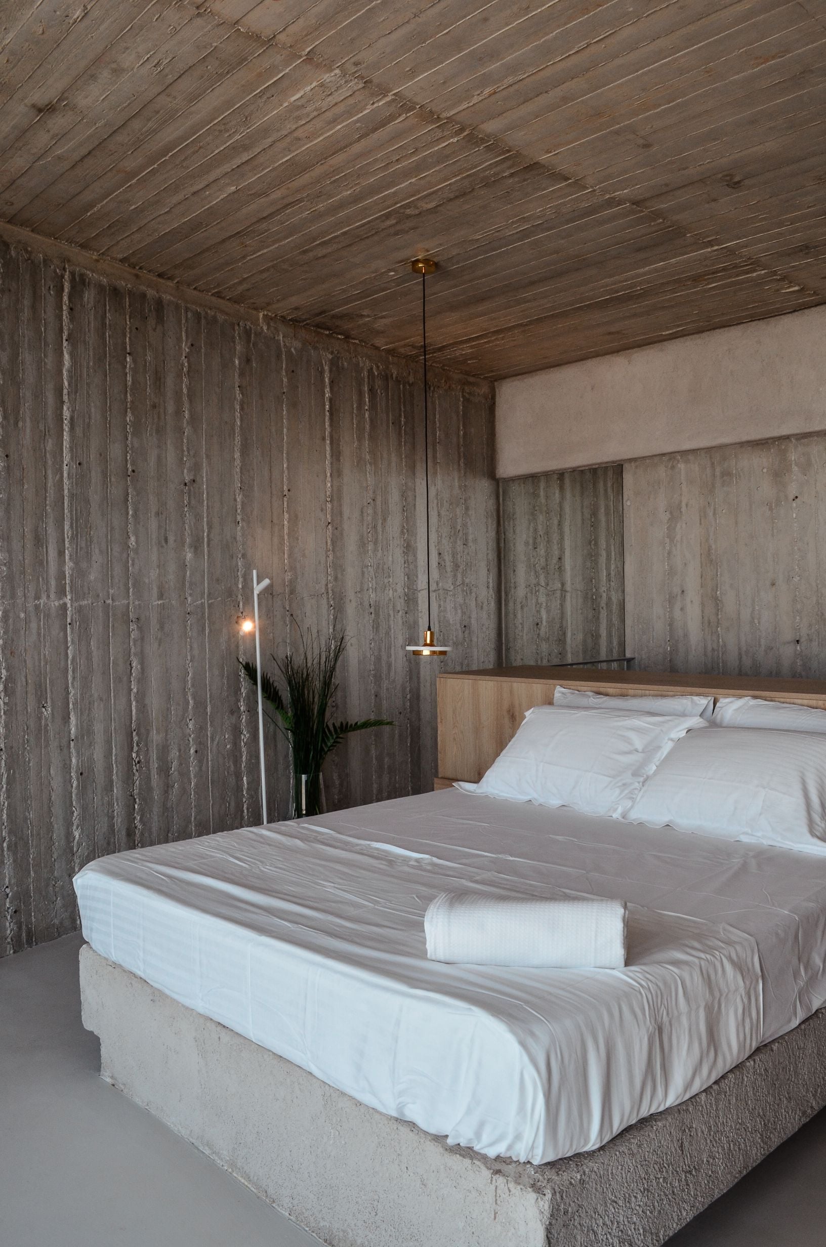 Bedroom with exposed concrete walls and ceiling and a low bed — Amoni